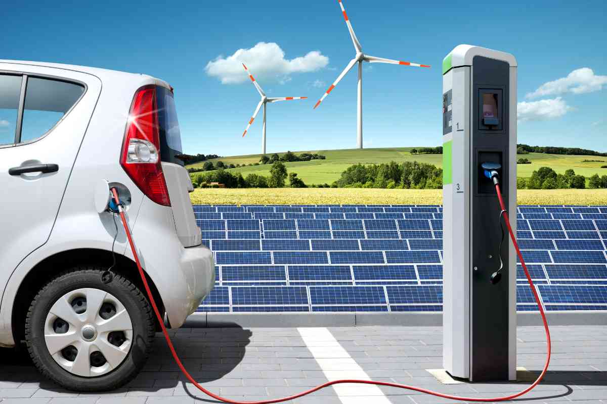 Ein Elektroauto an der Ladestation. Im Hintergrund sieht man ein Solarzellenfeld und zwei Windräder