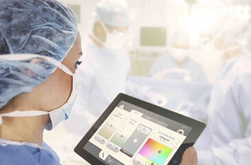 Eine medizinische Operation im Hintergrund. Im Vordergrund werden Daten über ein Tablet ausgelesen. Digitaler Wandel in der Medizintechnik