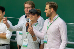 Eine Vortragende spricht und gestikuliert mit AR-Brille während ihr ein Mikrofon hingehalten wird. Datenorientierte Wertschöpfung