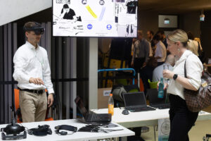 Ein Augmented-Reality Demonstrator wird von einem Mann in weißem Hemd bedient. Eine Frau beobachtet die Ergebnisse am Laptop mit Interesse