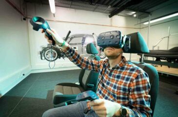 Ein Mann mit Virtual Reality-Brille sitzt in einem Fahrsimulator und bedient diesen. Virtuelle Realität