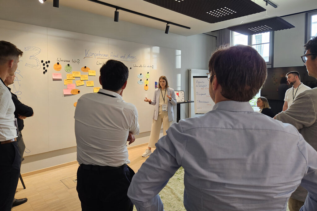 Austausch beim Kick-off des DaWeNa-HUB: Drei Teilnehmende stehen vor einer großen Wand voller Post-its, die Ideen skizzieren.