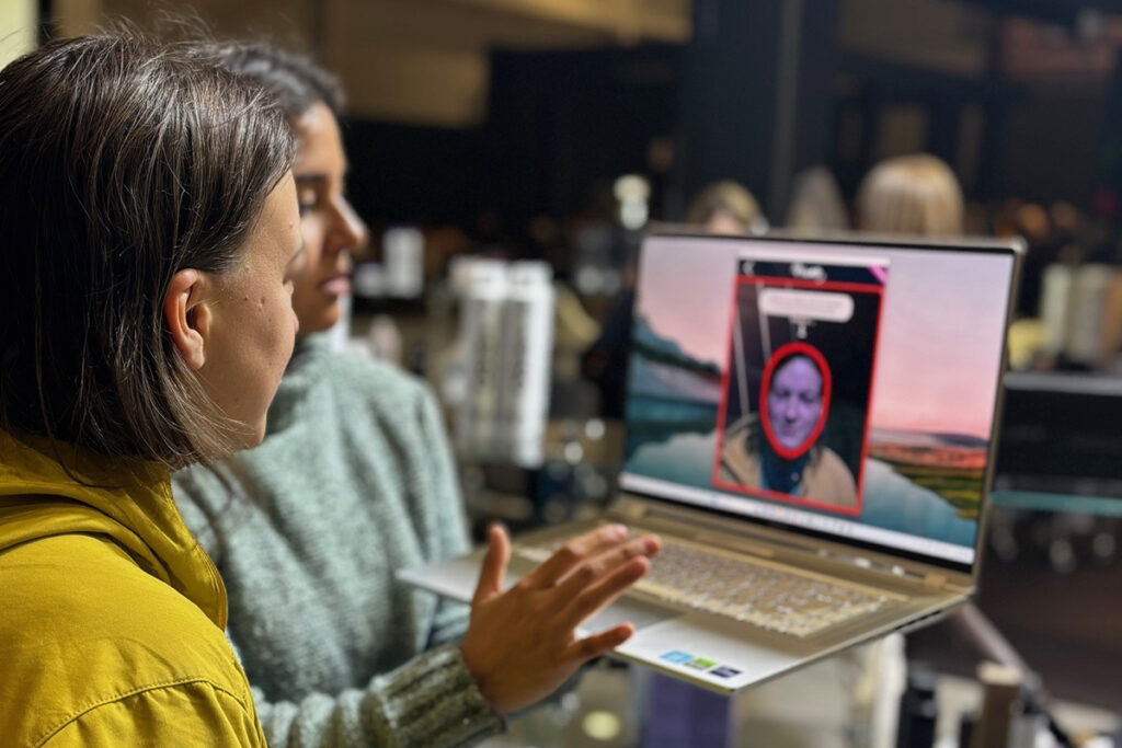 Zwei Frauen stehen auf der Messe vor einem Laptop und sehen sich das Ergebnis der FrisAR App auf dem Bildschirm an