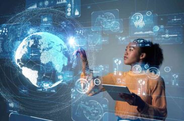 Eine Frau mit einem Tabloid arbeitet an einem großen Touchscreen, auf dem Diagramme, Roboterarmzeichnungen und die Weltkugel eingeblendet sind.