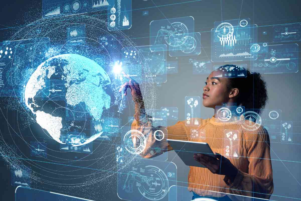 Eine Frau mit einem Tabloid arbeitet an einem großen Touchscreen, auf dem Diagramme, Roboterarmzeichnungen und die Weltkugel eingeblendet sind.