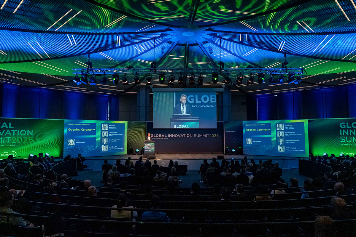 Ein Redner steht auf einer Bühne in einem großen runden Saal und eröffnet die Veranstaltung EUREKA Global Innovation Summit 2025