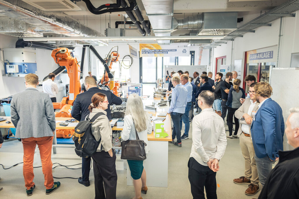 Besucher des SAAM Forum informieren sich in der Ausstellung der Fachkonferenz und betrachten die Demonstratoren bei der Erstellung großer Metallbauteile.