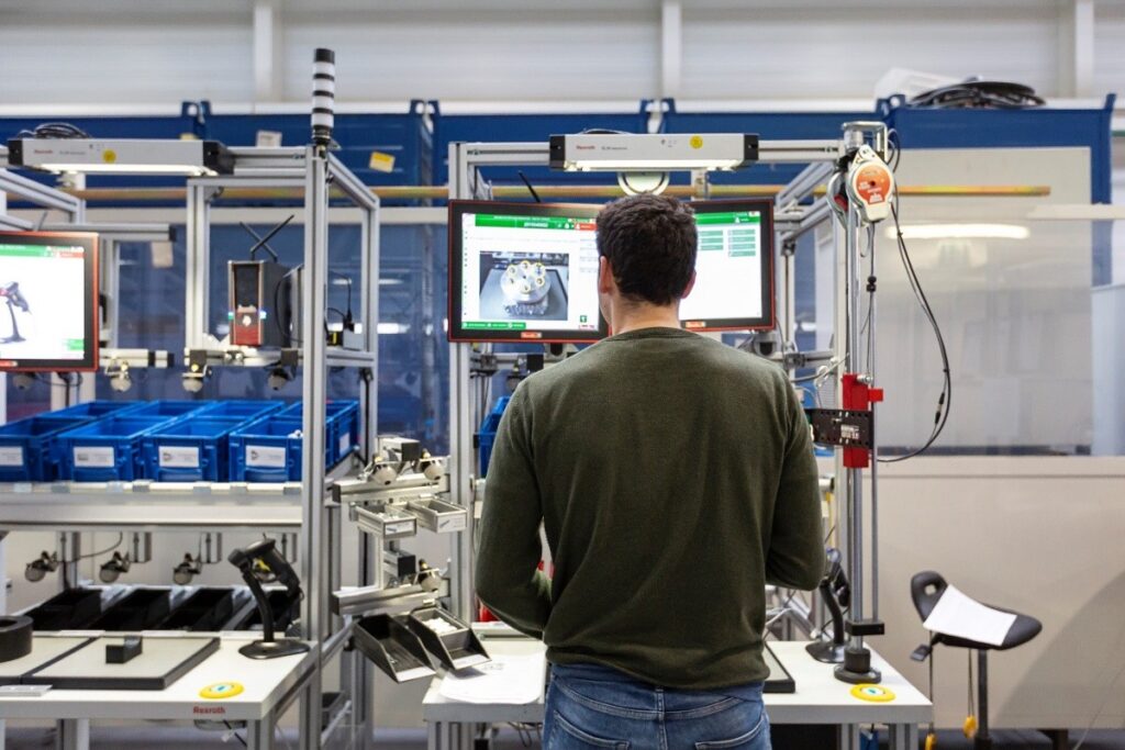 KompAKI Projektbild. Ein mann steht an einer Produktionseinheit und sieht auf einen Bildschirm. Auf dem Bildschirm werden Informationen angezeigt, damit er bei seiner Arbeit unterstützt wird.