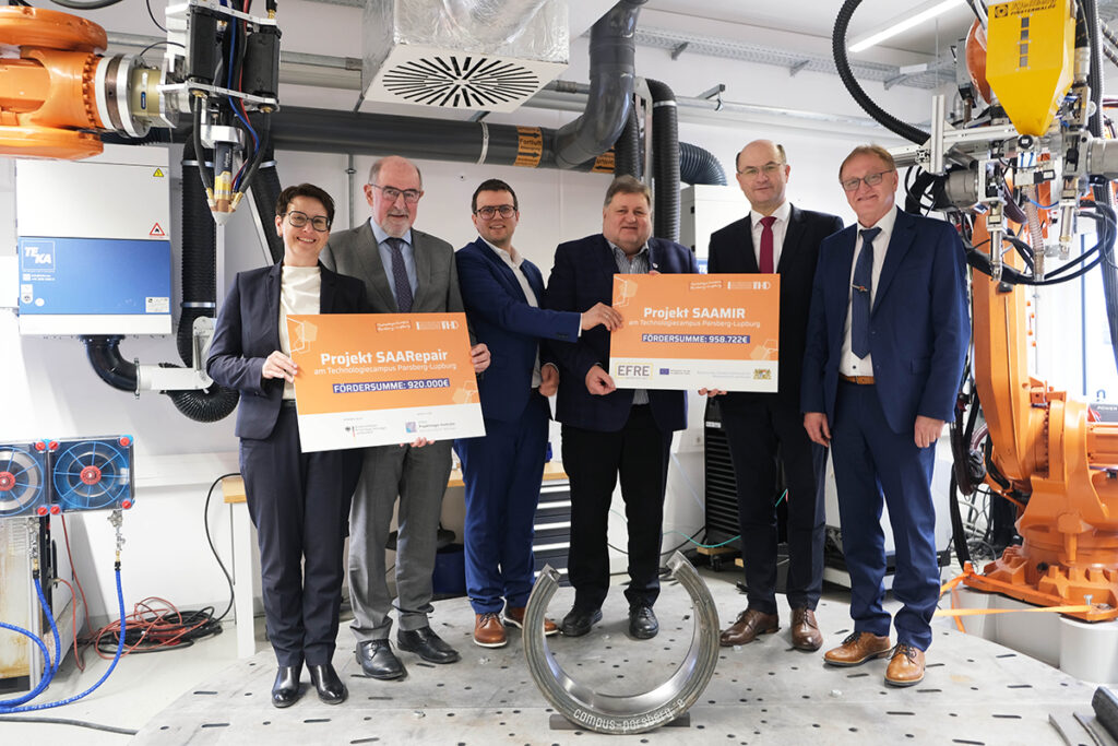 Gruppenbild: Vertretende des Bundesforschungsministeriums übergeben den Projektkoordinatoren der neuen geförderten Forschungsprojekte SAARepair und SAAMIR symbolisch Förderurkunden zum Start der Projektlaufzeit.